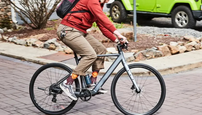 Enjoying the benefits of electric bikes: a person rides a sleek e-bike past a green Jeep, showcasing an eco-friendly commute.