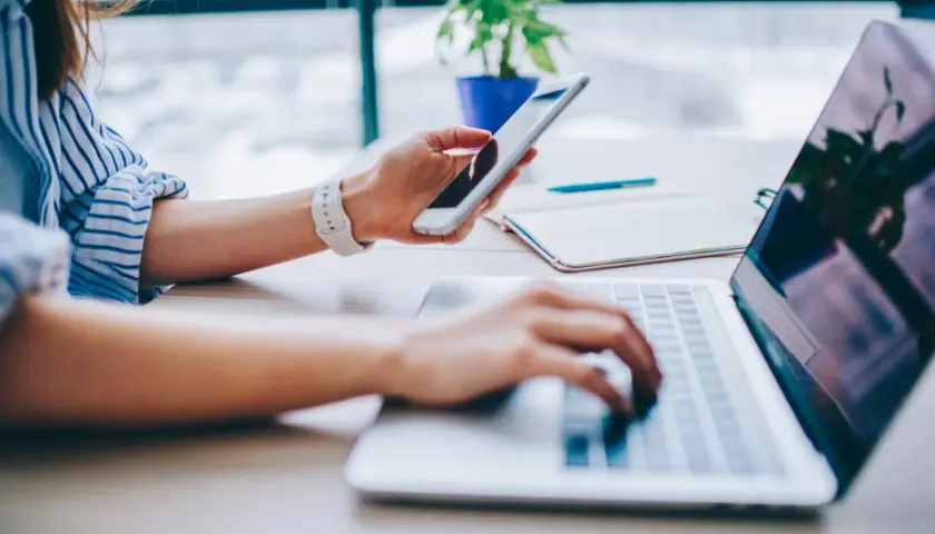 Kobieta korzysta z telefonu i laptopa, szukając informacji, jak podłączyć internet z telefonu do komputera.