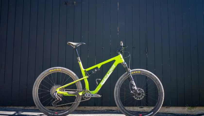 A bright green Santa Cruz Blur mountain bike is ready for a trail review, leaning against a dark wooden wall.