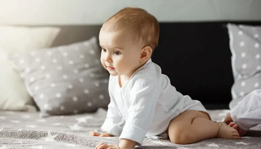 Urocze dziecko w białym body, kiedy dziecko raczkuje, z zaciekawieniem spogląda w bok.