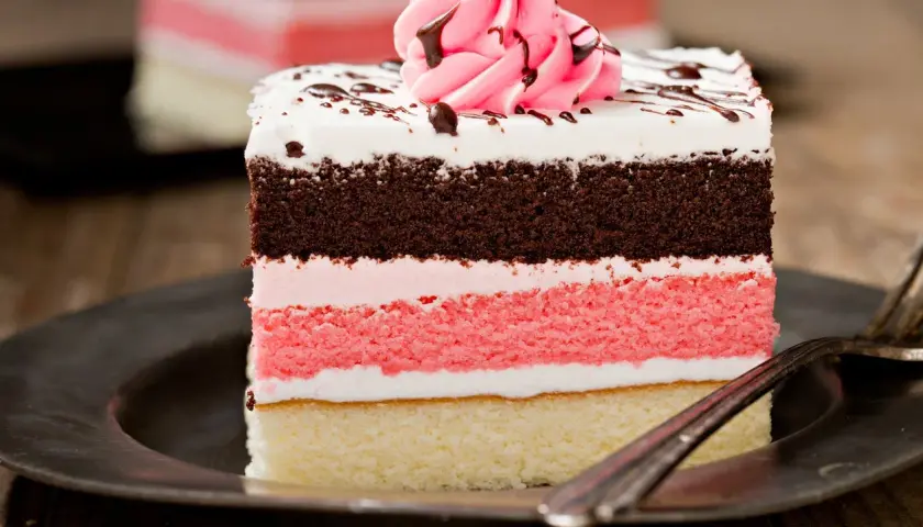 Un delicioso pastel napolitano en capas, con bizcocho de chocolate, fresa y vainilla, cubierto de crema y glaseado.