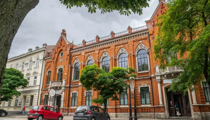 Ulica w Radomiu i okolicach z zabytkowymi kamienicami, drzewami i zaparkowanymi samochodami.