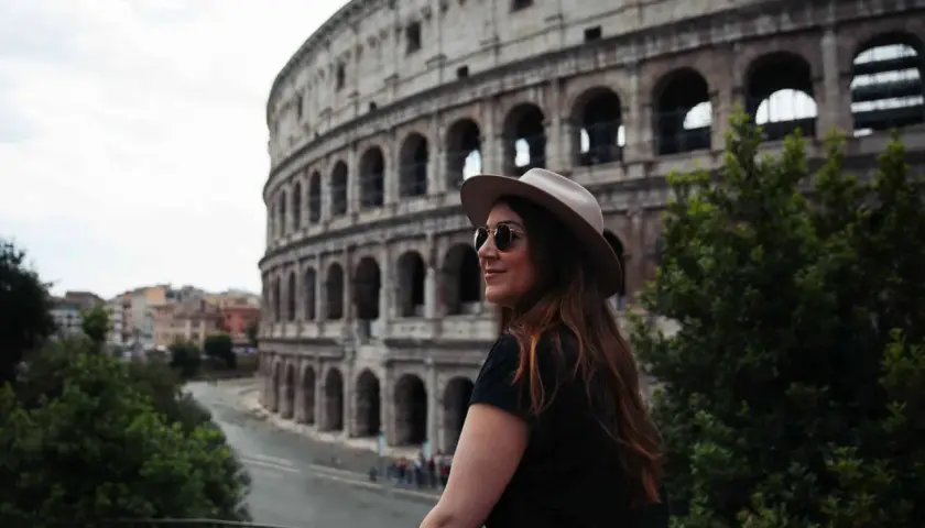 Une femme avec un chapeau et des lunettes de soleil admire le Colisée. Je visite Rome et ce moment est inoubliable.