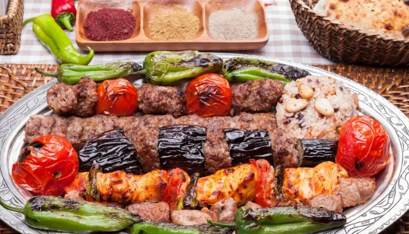 Turecka potrawa: grillowane mięso, bakłażany, pomidory i papryka na talerzu, obok ryż i pieczywo.