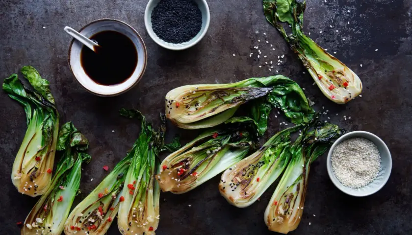 Grillad pak choi med sesamfrön och chili. En skål med sojasås och en skål med svarta sesamfrön syns också.