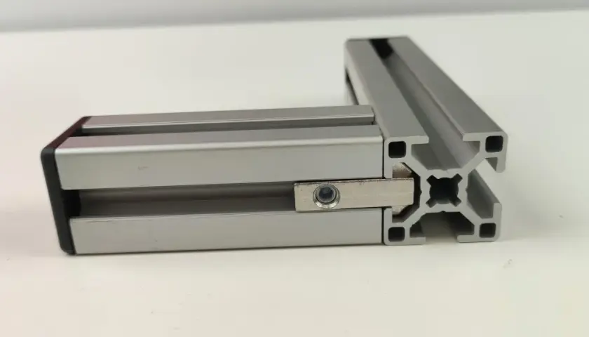 Dwa połączone profile aluminiowe konstrukcyjne tworzą kąt prosty. Widać element łączący z nakrętką.
