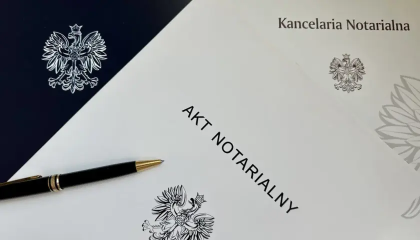 Na stole leży długopis obok dokumentu z napisem "AKT NOTARIALNY" i godłem Polski.