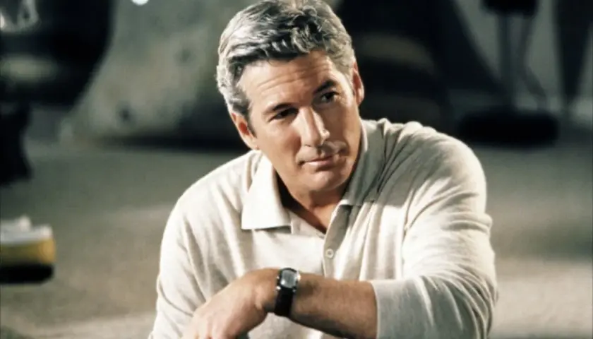 Hombre de pelo gris, con camisa clara y reloj, mira pensativo.