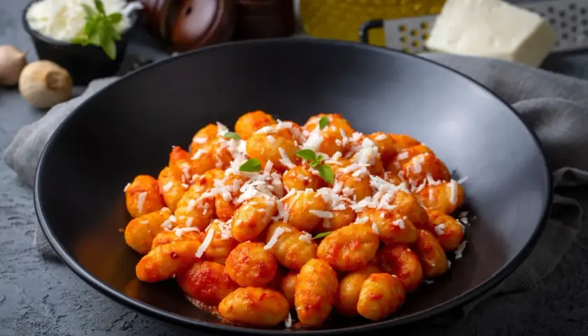 Gnocchi di ceci e patate conditi con sugo rosso e parmigiano grattugiato, guarniti con basilico fresco.
