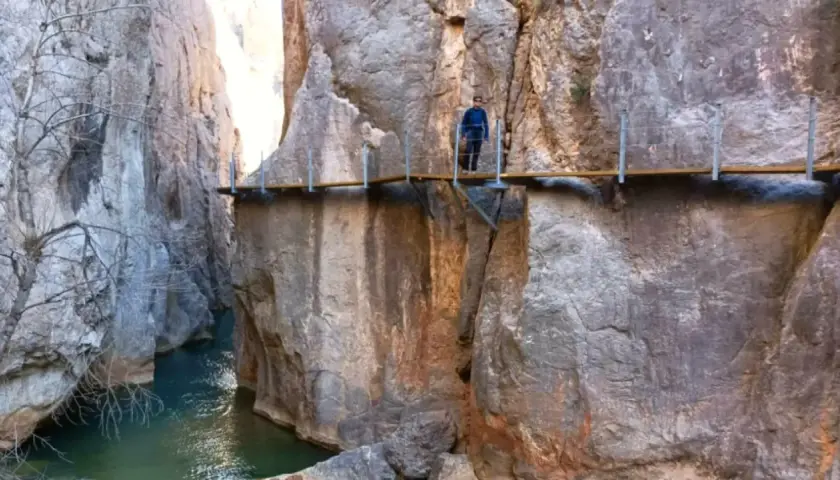 Un excursionista camina por las pasarelas de Valloré, un sendero suspendido sobre un río turquesa entre imponentes paredes rocosas.