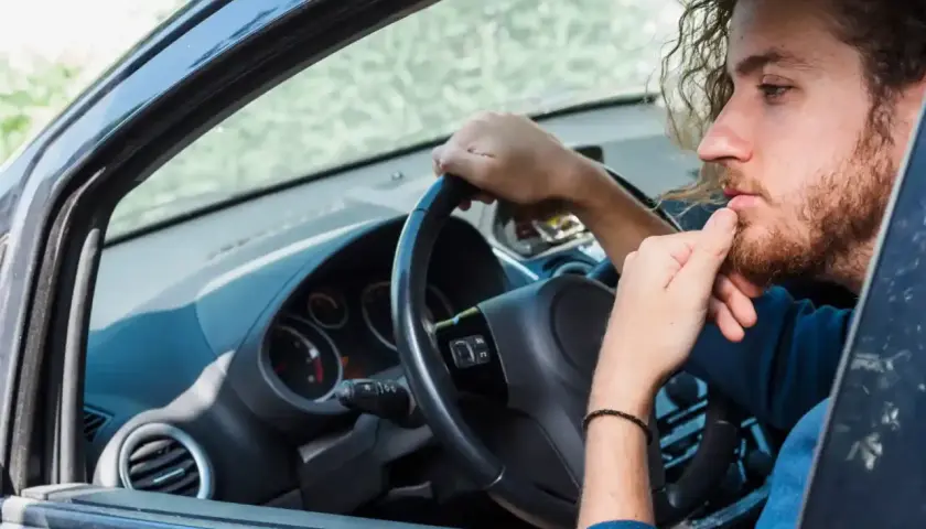 Hombre con barba y pelo rizado, pensativo, con la mano en la barbilla, mientras gira el volante y escucha un **ruido clack clack al girar el volante en parado**.