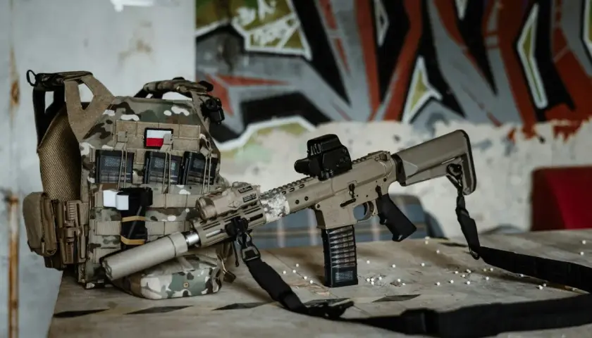Kamizelka taktyczna z polską flagą i karabin ASG g3, gotowe do akcji na tle graffiti.