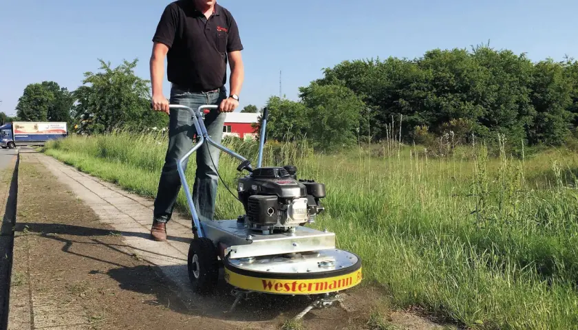 Mann mit Westermann Wildkrautbürste auf einem Gehweg, um Unkraut zu entfernen.