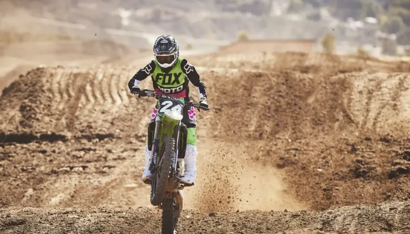 Motocrossowy zawodnik w stroju z logo Fox, jak prawdziwy fox titan, pędzi po piaszczystym torze, wzbijając tumany kurzu.