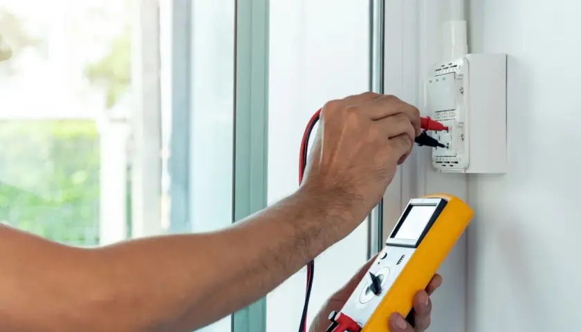 Elektryk wykonuje pomiar impedancji pętli zwarcia za pomocą żółtego miernika.