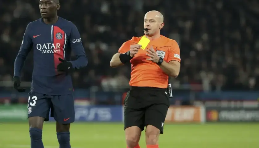Sędzia pokazuje żółtą kartkę piłkarzowi PSG.