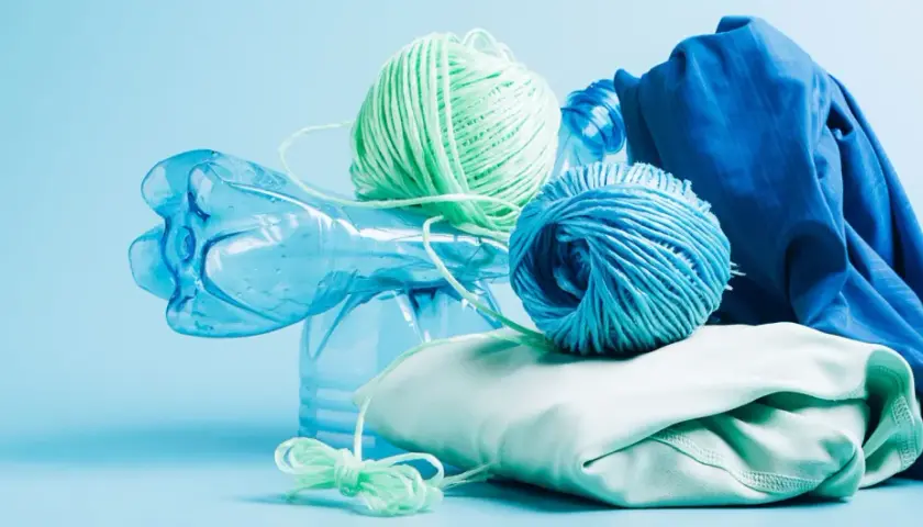 Bouteille en plastique bleue, pelotes de fil vert et bleu, et tissu bleu et vert pâle. Le fil est fait de polyester fiber, prêt à être recyclé.
