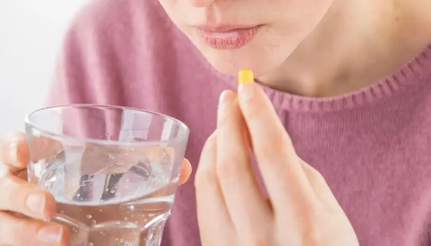 Frau nimmt Kapsel mit Wasser ein, hofft auf Linderung von Tinnitus durch Ashwagandha.