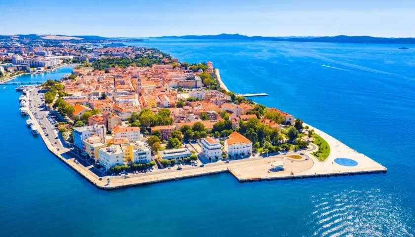 Widok z lotu ptaka na zabytkowe miasto Zadar z czerwonymi dachami, otoczone błękitnym morzem.