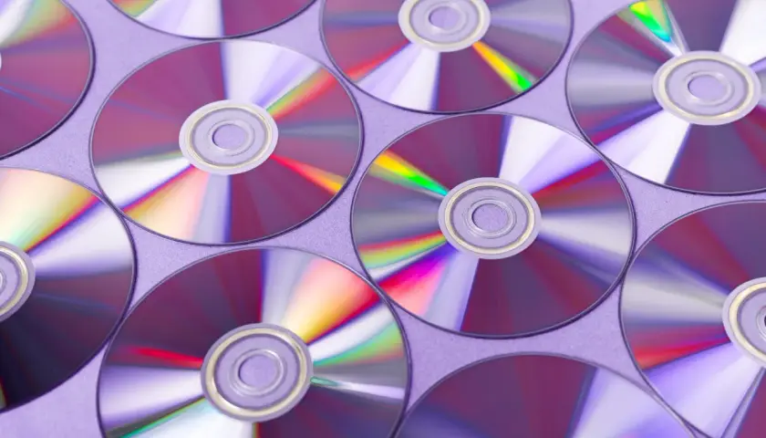 Płyty CD ułożone na fioletowym tle, odbijające światło.