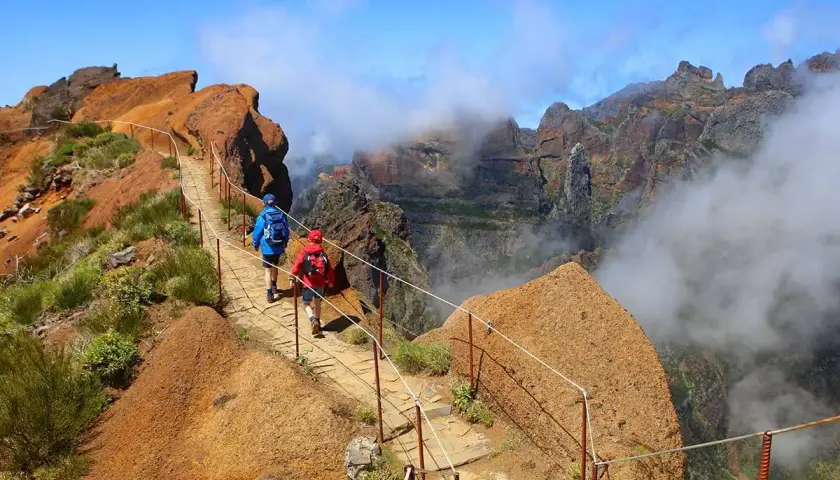 Hikers on a mountain path, a perfect example of things to do in Madeira. Dramatic cliffs and clouds surround them.
