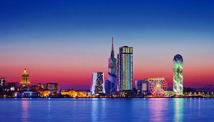 Widok na nowoczesną panoramę Batumi, stolicę Adżarii, o zachodzie słońca. Błyszczące wieżowce i diabelski młyn odbijają się w spokojnej wodzie.