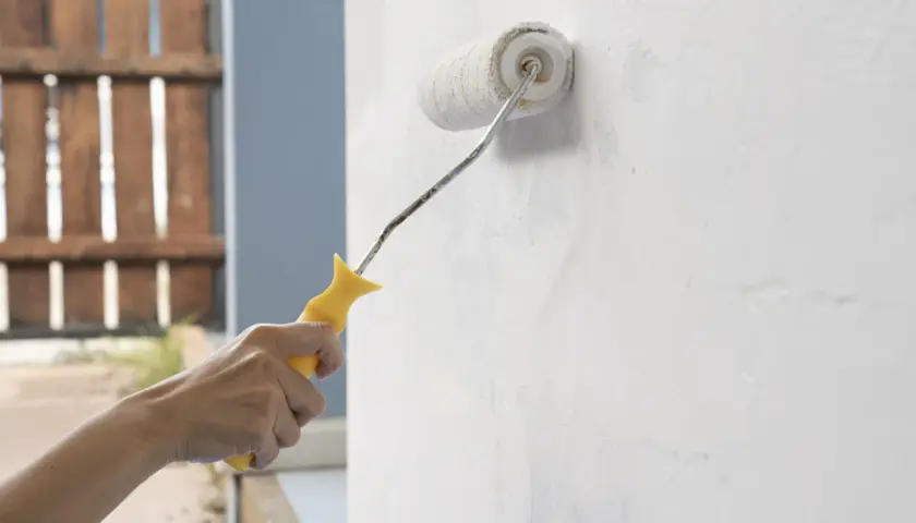 Mano aplica imprimación blanca a una pared con un rodillo. Se puede dar imprimación encima de pintura para un mejor acabado.