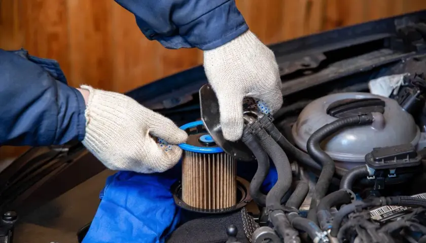 Ręce w rękawiczkach dokonują wymiany filtra paliwa diesel. Nowy element jest gotowy do montażu.