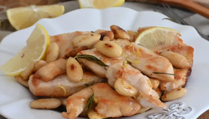Succulento pollo al limone con mandorle tostate e rosmarino, guarnito con spicchi di limone fresco.