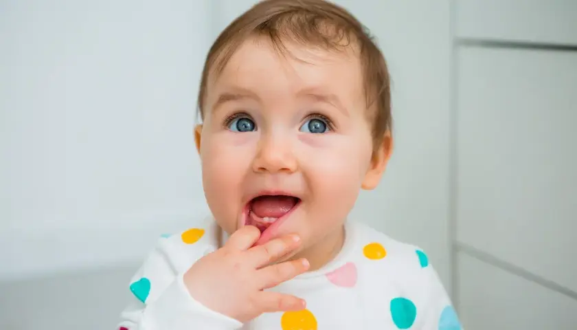Bambino con dentizione neonato sintomi, che si porta il dito alla bocca con un'espressione curiosa.