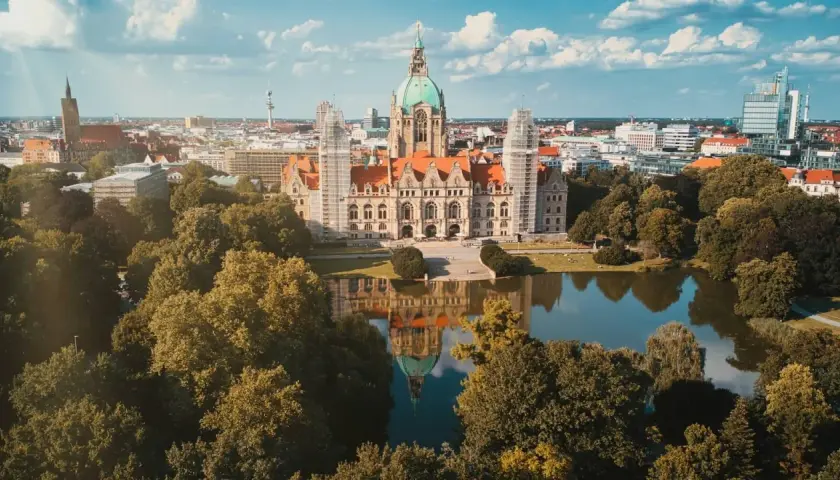 Nowy Ratusz w Hanowerze, stolicy Dolnej Saksonii, odbija się w spokojnej tafli jeziora, otoczony zielenią drzew.