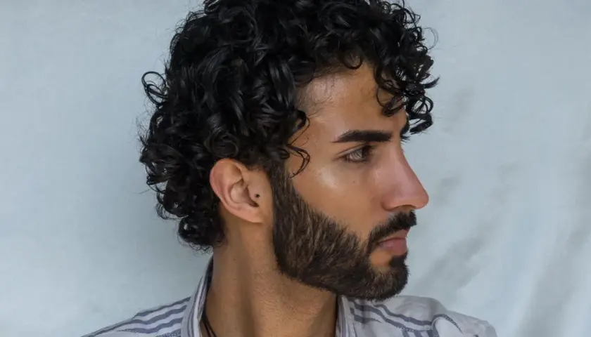 Perfil de hombre con pelo ondulado oscuro y barba cuidada.