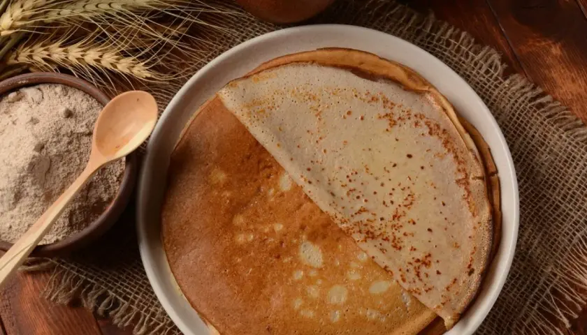 Crêpes dorées faites avec de la farine semi-complète, prêtes à être dégustées. À côté, un bol de farine et des épis de blé.