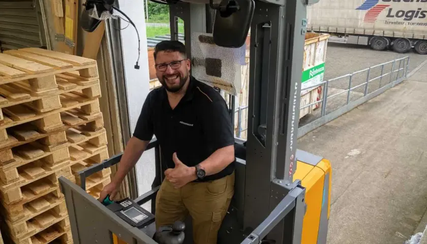 Mann gibt Daumen hoch in einem Hochhubwagen, bereit für die Stapler Unterweisung. Paletten stapeln sich links.