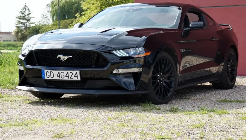 Czarny Ford Mustang z polską tablicą rejestracyjną stoi na żwirowej nawierzchni.