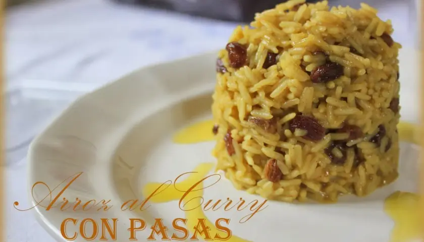 Arroz al curry con pasas, un plato aromático y dulce servido en un plato blanco con un toque de salsa dorada.