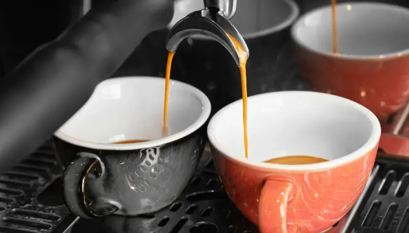 Dwa kubki, jeden czarny, drugi czerwony, napełniane są gorącym, aromatycznym espresso doppio.