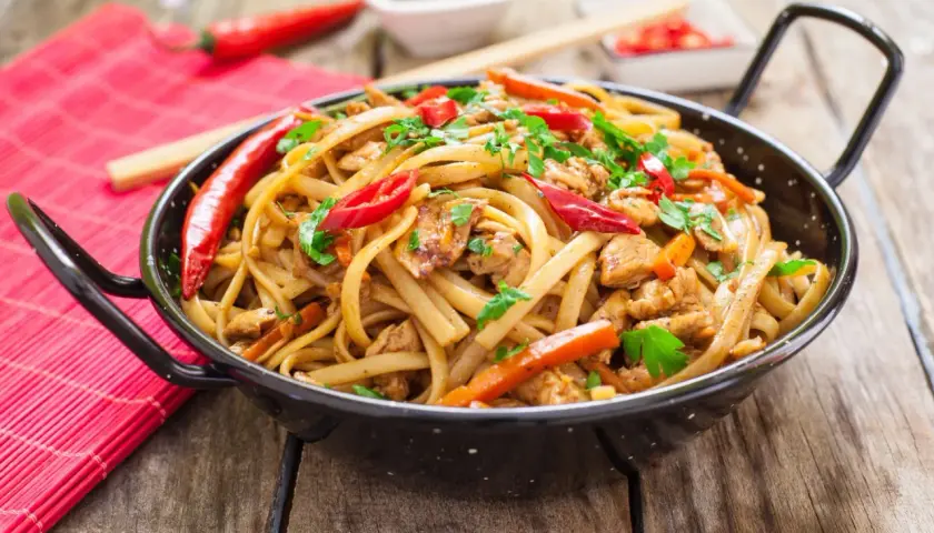 Pyszny makaron chow mein z kurczakiem, papryką i chili, posypany świeżą pietruszką.