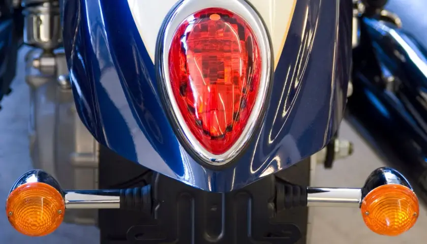 Detalle de moto azul con luces LED naranjas y piloto trasero rojo. Podría ser una multa por llevar luces LED en moto.