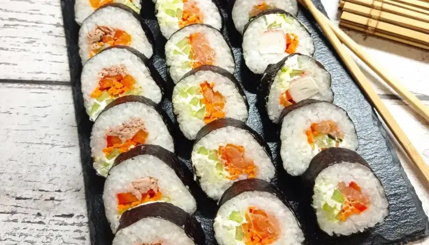 Pyszne domowe sushi z łososiem, tuńczykiem i warzywami, ułożone na czarnej desce.