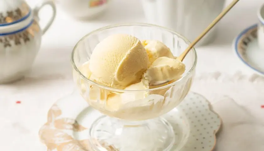 Copa de cristal con helado de mantecado cremoso, servido con una cuchara dorada.