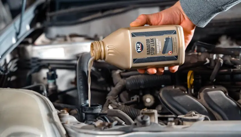 Dłoń wylewa płyn do chłodnicy z butelki K2 Radiator Stop Leak, wykonując wymianę płynu chłodniczego.