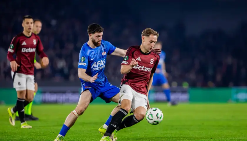 Piłkarze w akcji podczas meczu sparta praga: rozgrywki. Jeden z nich w bordowej koszulce walczy o piłkę z rywalem w niebieskim stroju.