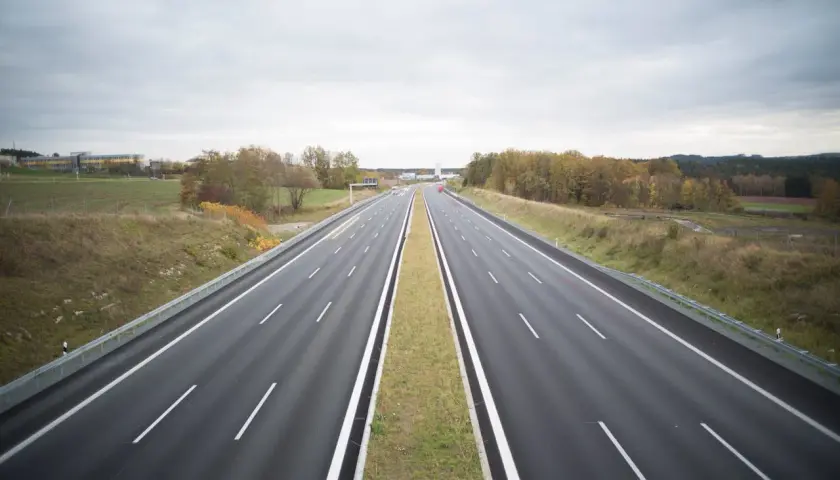 Pusta autostrada w Niemczech, gdzie podróżowanie jest bezpłatne. W oddali widać budynki i jesienne drzewa.