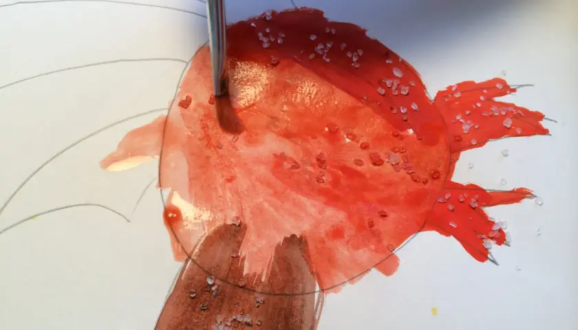 Ein Pinsel trägt rote Farbe auf, während grobes Salz auf dem nassen Aquarellpapier liegt. Diese Salz-Bilder entstehen durch die Reaktion von Salz und Farbe.