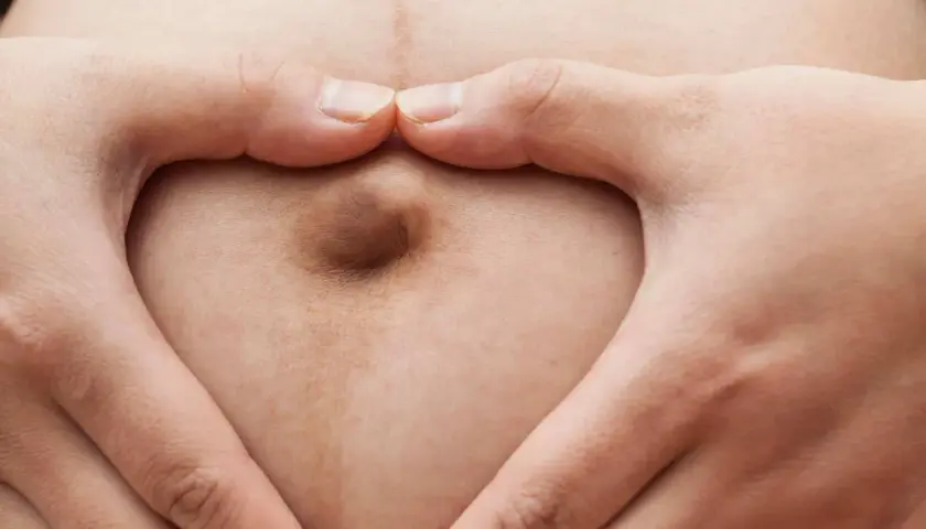 Mani a cuore circondano un ombelico in gravidanza, simbolo di amore e attesa.
