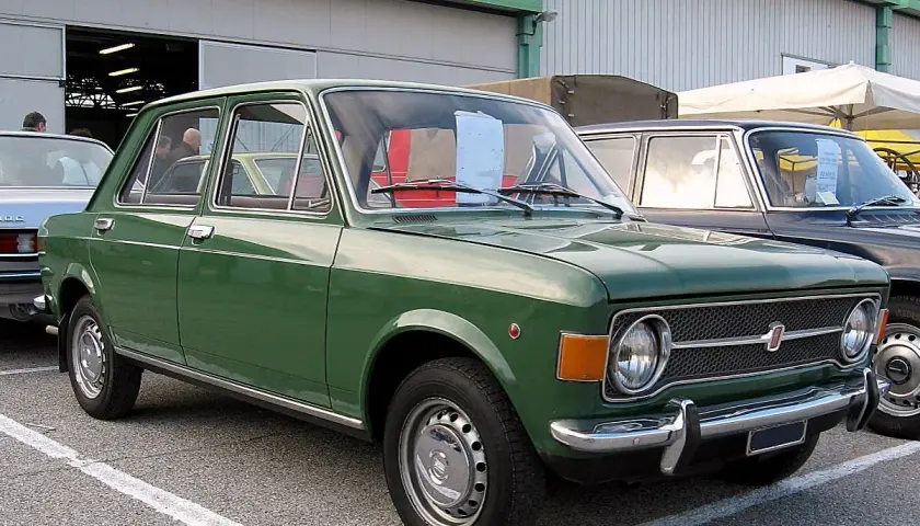 Zielony fiat 128, klasyk z lat 70., zaparkowany przed budynkiem.