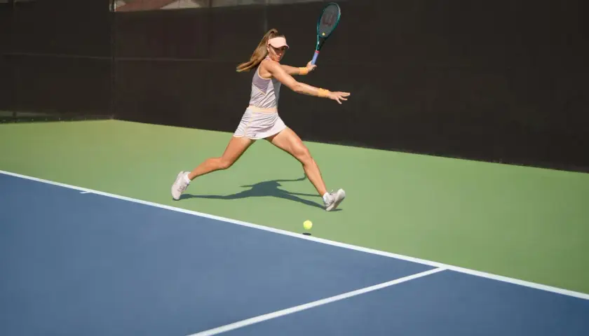 Kobieta w ruchu na korcie tenisowym, uderzająca piłkę. Widać jej determinację i przewagę w tenisie.