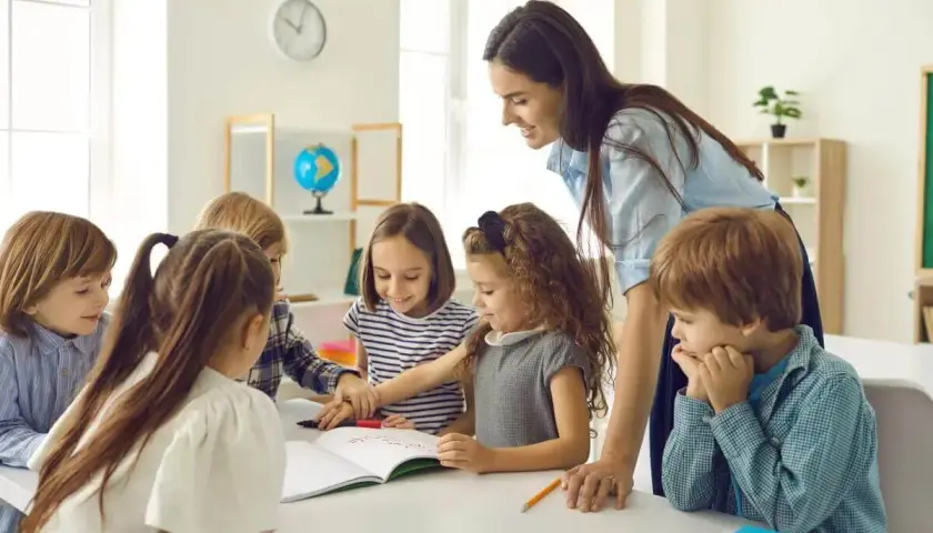 Lehrerin unterstützt Kinder bei ihrer Projektarbeit. Sie arbeiten gemeinsam an einem Buch, lernen und lachen.