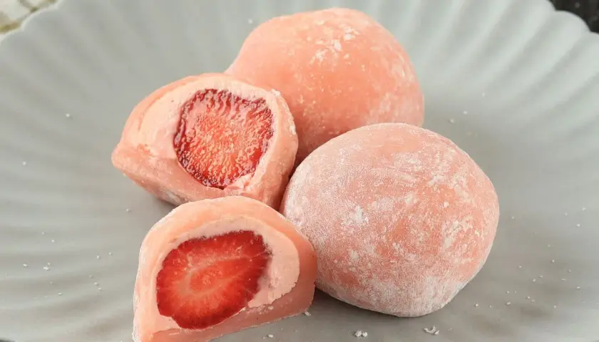 Różowe mochi z truskawkami na szarym talerzu.